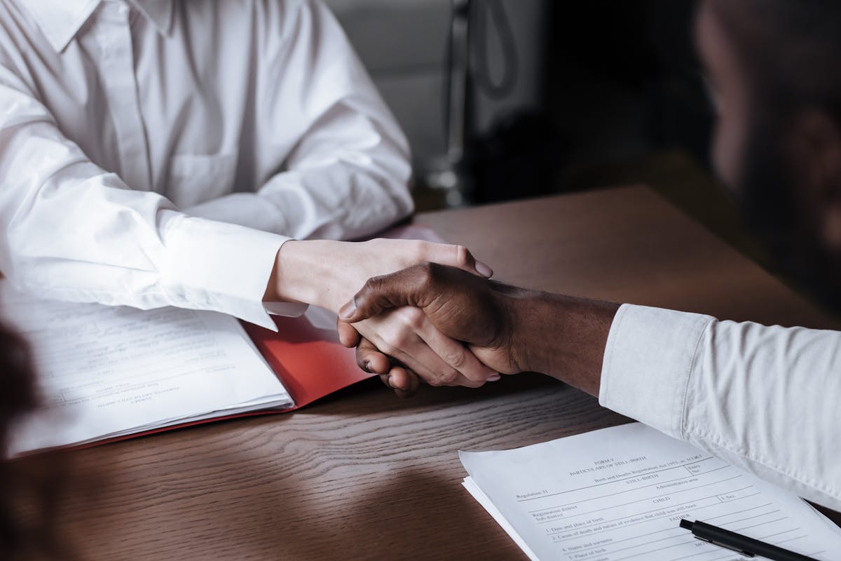 A handshake over documents at a desk.